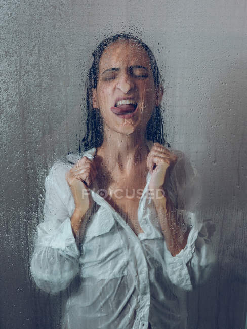 Frau im Hemd posiert mit ausgestreckter Zunge in Duschkabine — Stockfoto