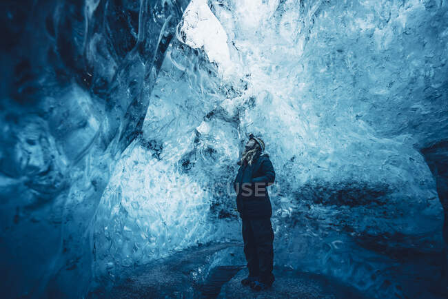 Traveling man in outwear standing in crystal blue ice cave looking up, Iceland — Stock Photo