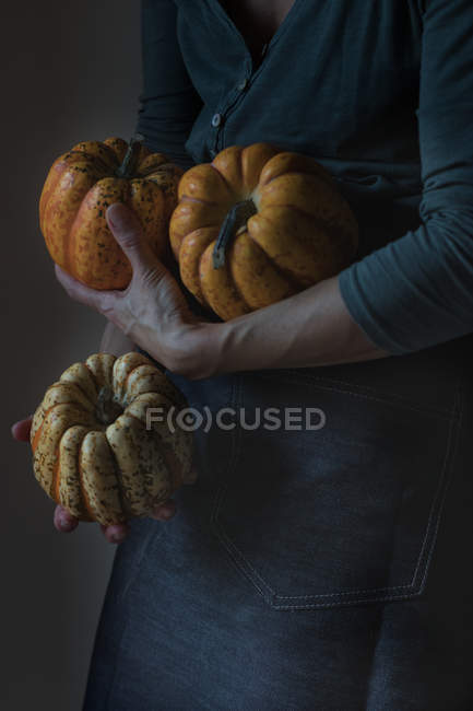 Unrecognizable woman holding three tiny pumpkins as standing on gray background — Stock Photo