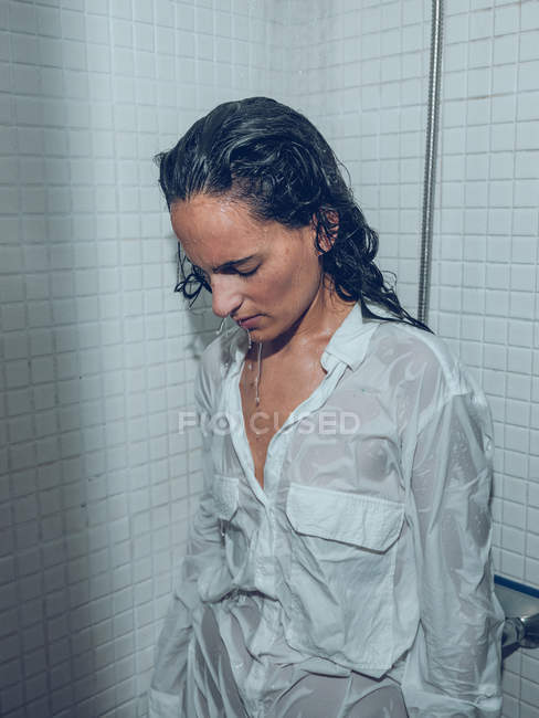 Attraktive junge Frau im weißen nassen Hemd steht unter Wasserspray in der Dusche — Stockfoto