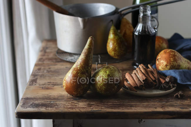 Fresh pears and various aromatic spices on lumber tabletop near bottle of wine and metal saucepan — Fotografia de Stock