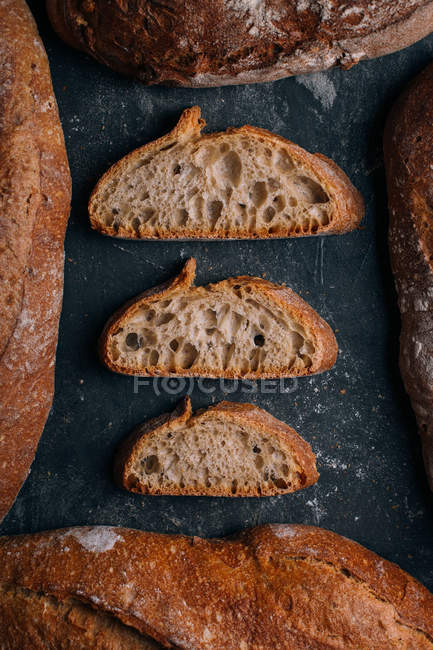 Homemade rustic bread loaves with slices on dark background — Stock Photo