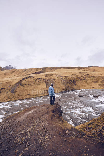 Vue latérale gars debout sur la pierre près de rivière coulant entre les montagnes brunes en Islande — Photo de stock