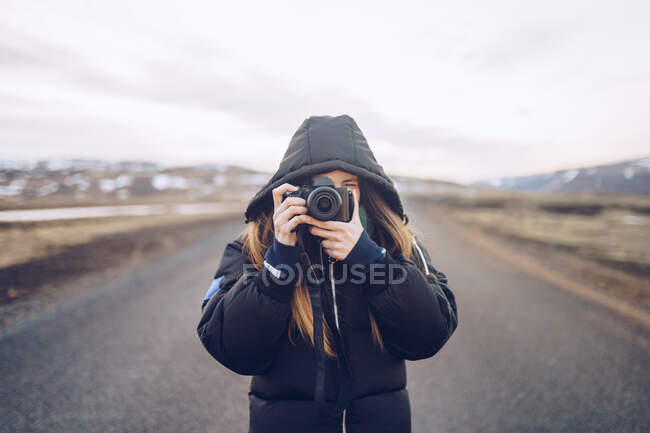 Молода жінка в лижній куртці дивиться через камеру на дорозі між дикими землями в Ісландії. — стокове фото