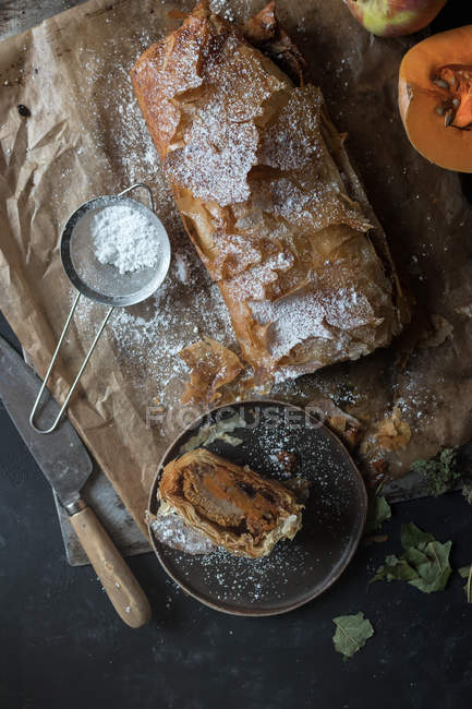 Homemade pumpkin and apple strudel on parchment with ingredients on dark background — Stock Photo