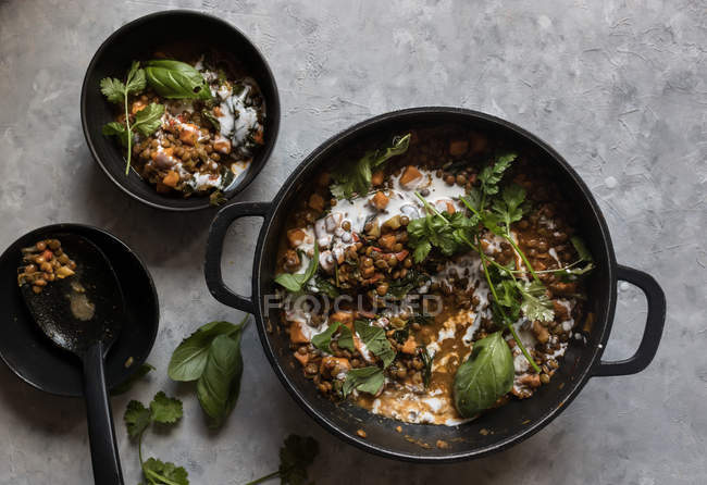 Topf Ragout mit Linsen-Süßkartoffel-Curry und Schüssel auf grauer Tischplatte — Stockfoto