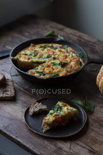 Plate and metal saucepan with delicious pumpkin and spinach frittata standing on timber tabletop — Stock Photo