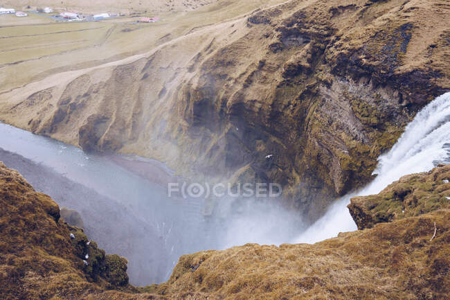 Desde arriba cascada de agua cayendo en el río de montaña entre colinas de piedra marrón en Islandia - foto de stock