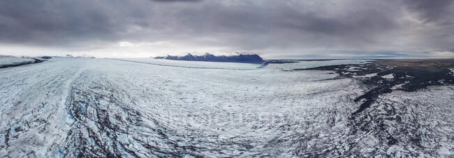 Panorâmica de ângulo largo tiro de terreno gelado branco com montanhas distantes à distância, Islândia — Fotografia de Stock
