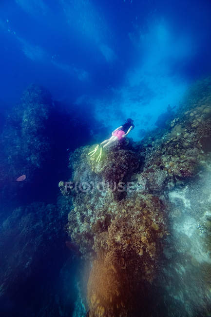 Человек ныряющий между рифами под водой в море — стоковое фото