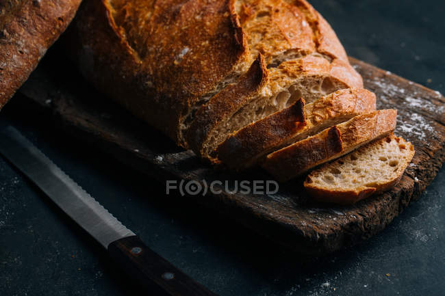 Partly sliced homemade rustic bread on wooden board — Stock Photo
