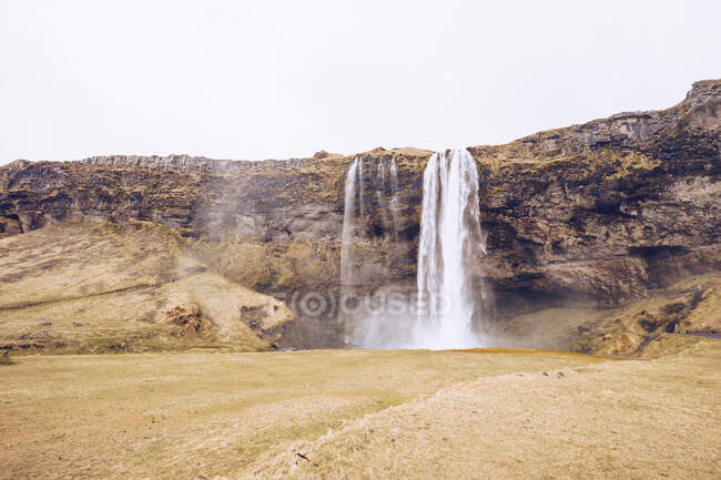 Каскад воды, падающий в реку между скалами Исландии — стоковое фото