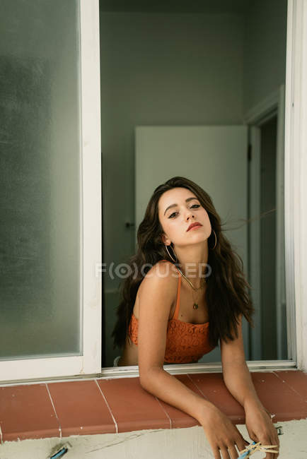 Passionate attractive brunette woman looking at camera, holding pins and leaning out from window — Stock Photo