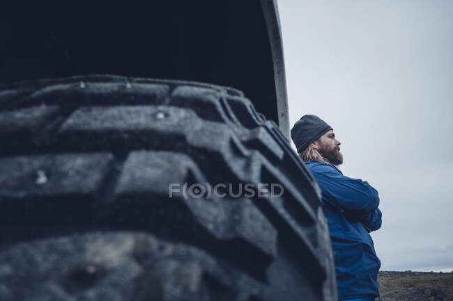 Von unten Seitenansicht eines Mannes, der sich auf einen riesigen LKW mit massiven Rädern lehnt und wegschaut, Island — Stockfoto