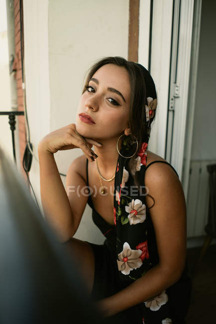 Charmante jeune femme en robe assise sur le balcon et regardant la caméra — Photo de stock