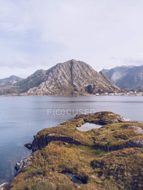 Paysage de montagnes rocheuses avec peu de végétation verte et d'eau claire tranquille, Îles Lofoten — Photo de stock