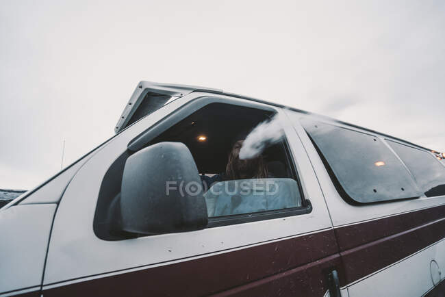 Desde abajo vista del hombre sentado dentro del coche y fumando mientras conduce, Islandia - foto de stock