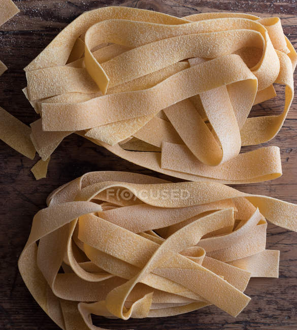 Heap of uncooked pappardelle spaghetti on wooden table — Stock Photo