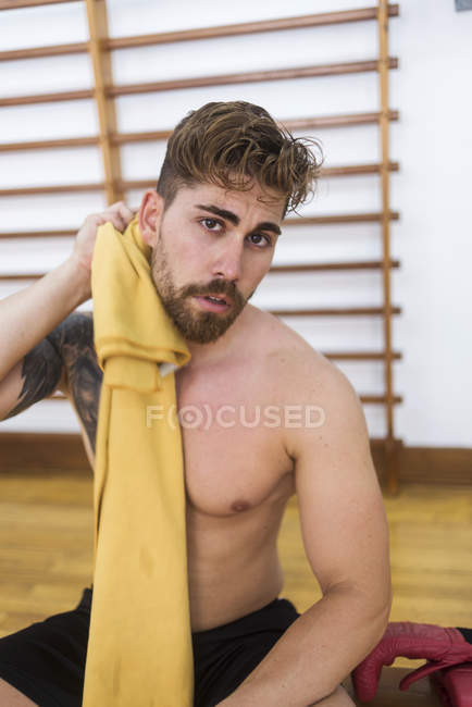 Hombre musculoso barbudo con toalla sentado después de entrenar en el gimnasio - foto de stock