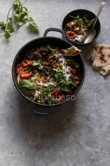 Olla de ragú con lentejas y batata al curry y un tazón en la mesa gris - foto de stock