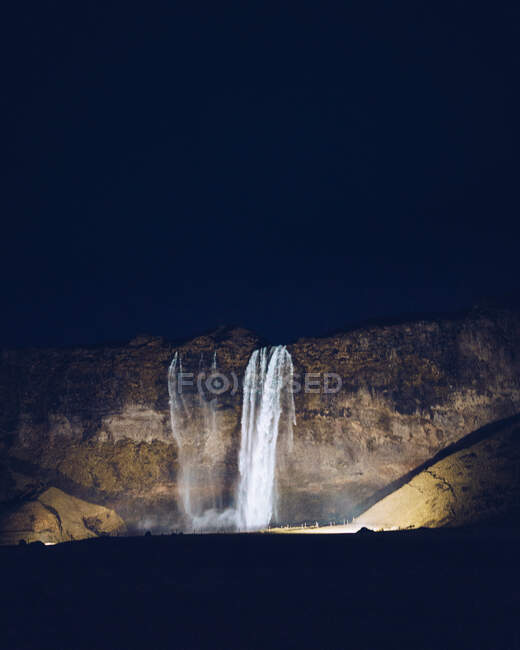 Cascata de água destacada caindo entre rochas na escuridão na Islândia — Fotografia de Stock