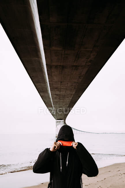 Парень в черной одежде держит пик и стоит на берегу под мостом над водой и облачное небо во Франции — стоковое фото