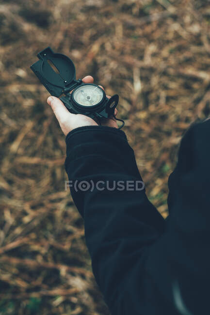 Jovem segurando uma bússola na montanha ao lado de um rio com fundo de cor marrom — Fotografia de Stock