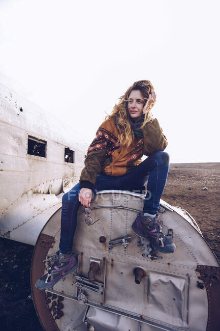 Jovem senhora no desgaste quente sentado em aeronaves quebradas entre terrenos escuros na Islândia — Fotografia de Stock