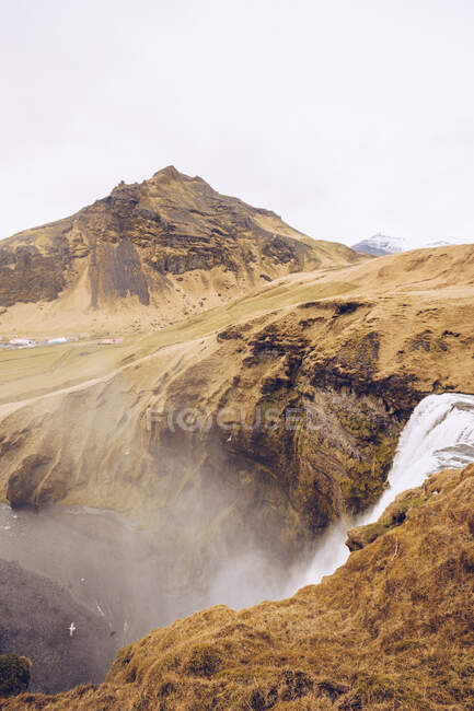 Rivière de montagne avec cascade d'eau entre collines de pierre brune et vue sur les plaines d'Islande — Photo de stock
