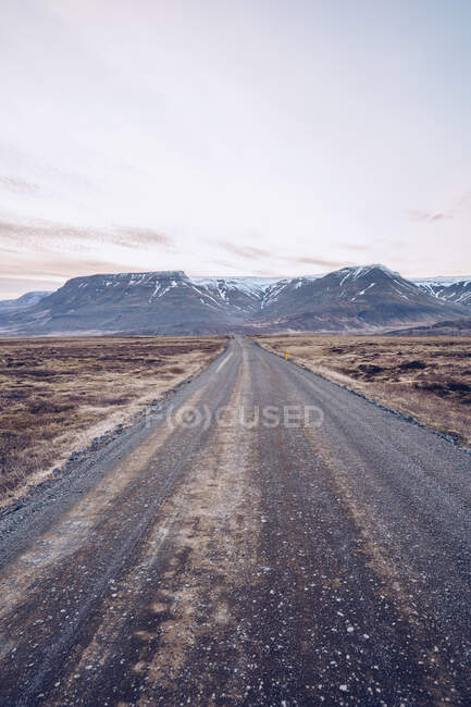 Деревенская дорога между дикими землями, ведущая к горам и красивому небу в Исландии — стоковое фото