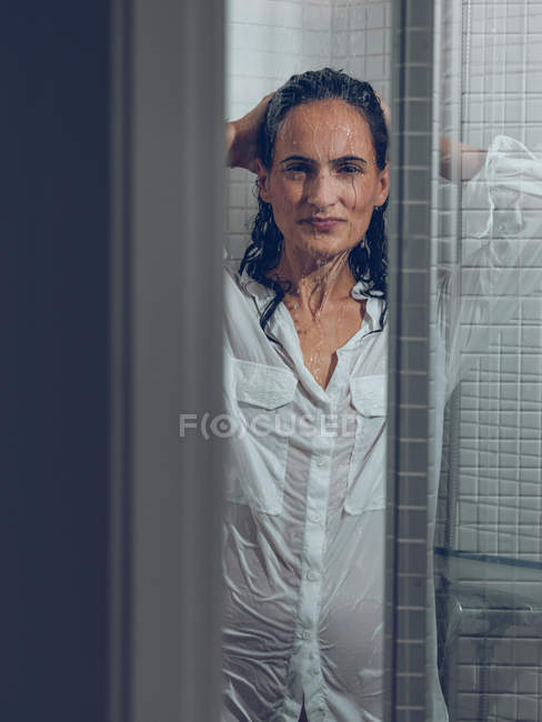 Esguichando mulher na camisa com as mãos no cabelo posando no chuveiro — Fotografia de Stock