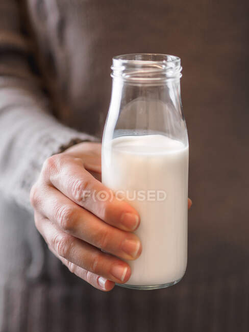 Primer plano de la mano de una mujer anónima sosteniendo una pequeña botella de leche fresca - foto de stock