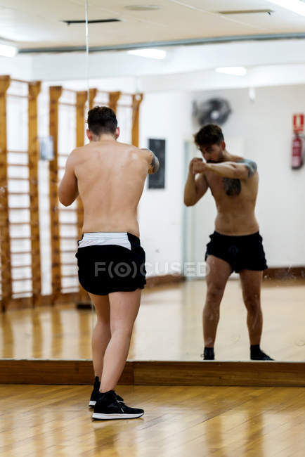 Bearded male fighter working out in gym against mirror — Stock Photo