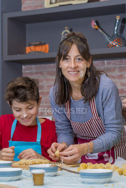 Mamá e hijo jugando con masa y harina mientras trabajan en pastelería en casa - foto de stock