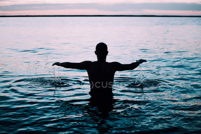 Retour gars vue debout dans l'eau avec les mains en l'air et le ciel rose en France — Photo de stock