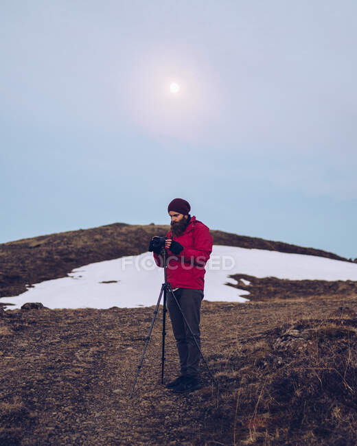 Young beard guy in ski jacket fixing camera on trip  and sunshine on blue sky in Iceland — Stock Photo