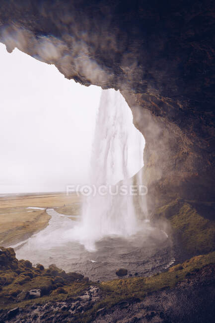 Cavern with water cascade falling in river streaming between wild lands in Iceland — Stock Photo