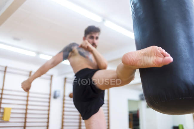 Kickboxing fighter training in palestra con sacco da boxe — Foto stock