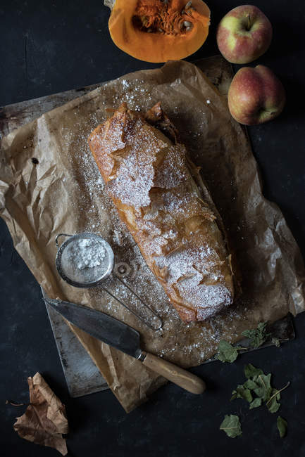 Zucca fatta in casa e strudel di mele su pergamena con ingredienti su sfondo scuro — Foto stock