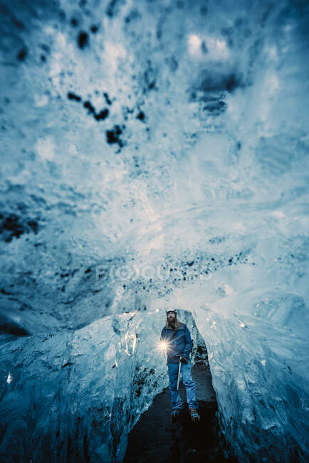 Traveler with burning torch standing in hall of crystal blue ice cave, Iceland — Stock Photo