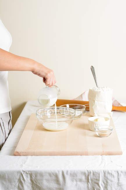 Cuenco de relleno femenino irreconocible con leche fresca mientras se cocina en la cocina . - foto de stock
