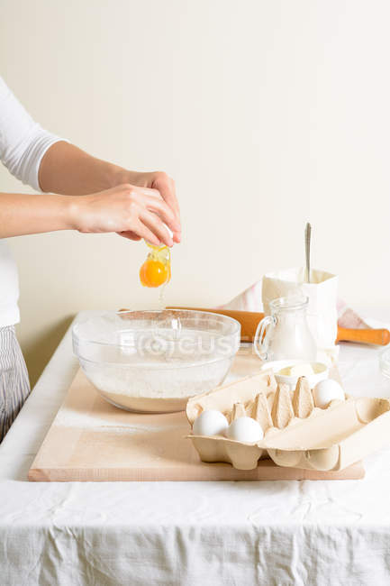 Ritagliato di donna versare l'uovo in ciotola durante la cottura in cucina . — Foto stock