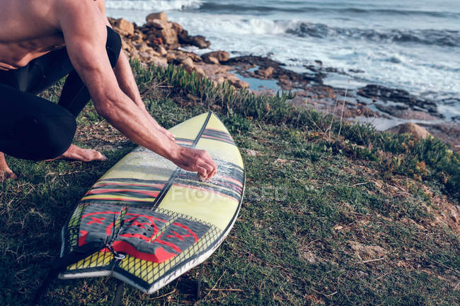 Nahaufnahme eines Mannes beim Putzen eines Surfbretts an der Küste des Ozeans — Stockfoto