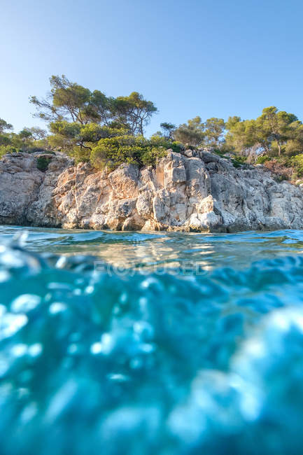 Scogliera con alberi vicino acqua di mare turchese — Foto stock