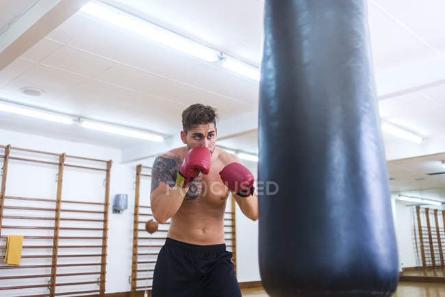 Junger Bärtiger trainiert mit Boxsack in Turnhalle — Stockfoto