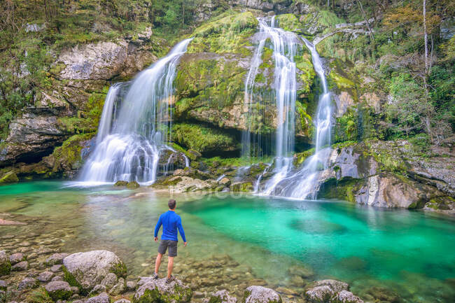 Back view guy standing on stone near beautiful waterfall and mountain river with azure clean water in Slovenia and Croatia — Fotografia de Stock