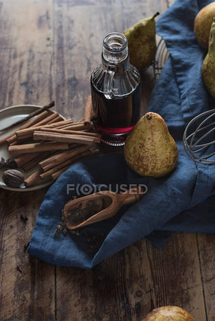 Par-dessus des poires mûres près d'une bouteille de vin rouge et d'une assiette aux épices aromatiques variées sur une table en bois — Photo de stock