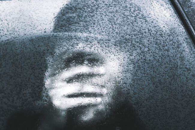 Silhouette of human in cap closing face by hand inside of car window with glare ice in France — Stock Photo