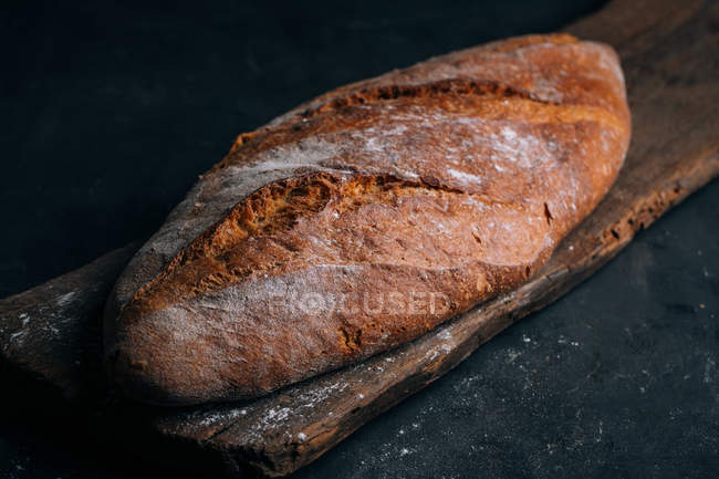 Hausgemachter rustikaler Brotlaib auf Holzbrett auf dunklem Hintergrund — Stockfoto