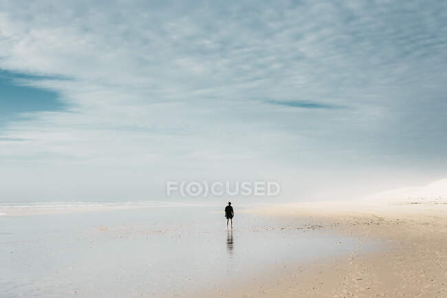 Человек на песчаном пляже возле воды и облачного неба — стоковое фото